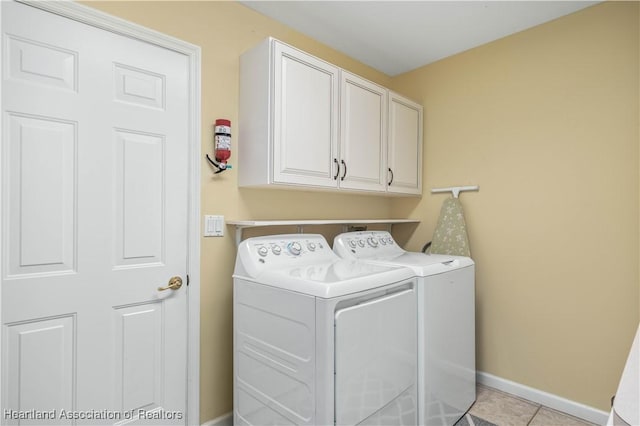 clothes washing area with cabinets, light tile patterned floors, and washing machine and clothes dryer