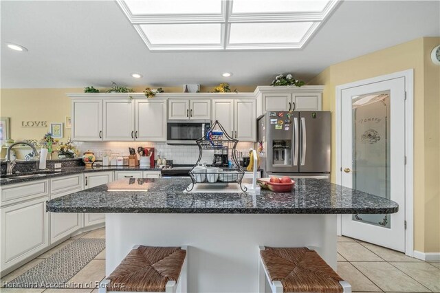 kitchen featuring sink, dark stone counters, a breakfast bar area, light tile patterned floors, and appliances with stainless steel finishes