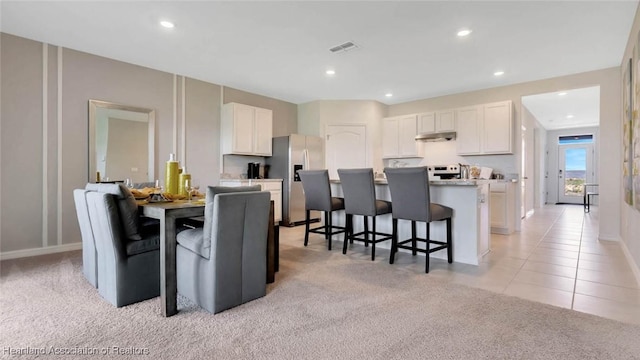 6836 Coconut Dr, Sebring, FL 33872 - kitchen featuring stainless steel fridge, under cabinet range hood, a breakfast bar area, white cabinetry, and an island with sink