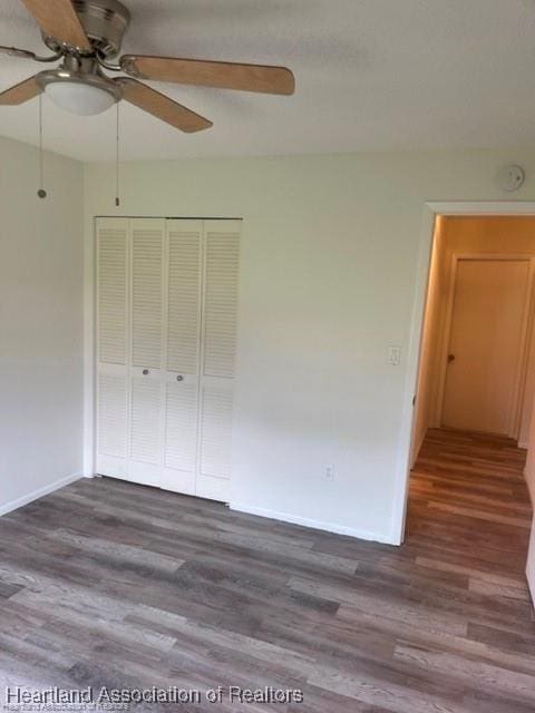 unfurnished bedroom with ceiling fan, dark wood-type flooring, and a closet