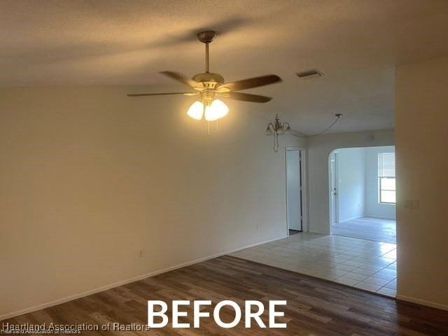 empty room with baseboards, visible vents, dark wood finished floors, arched walkways, and ceiling fan