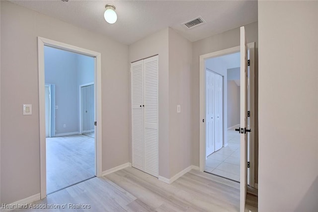 corridor with visible vents, light wood finished floors, and baseboards