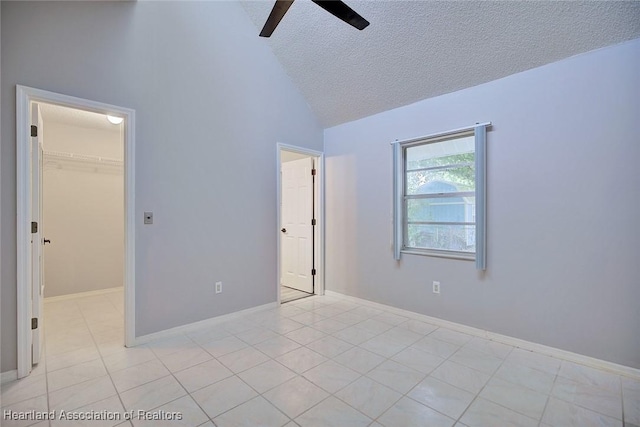 unfurnished bedroom with lofted ceiling, a textured ceiling, light tile patterned floors, a spacious closet, and a ceiling fan