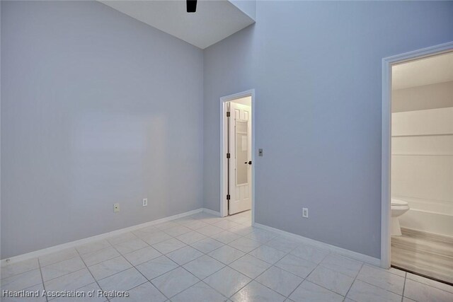 unfurnished bedroom with light tile patterned floors, baseboards, and ensuite bathroom