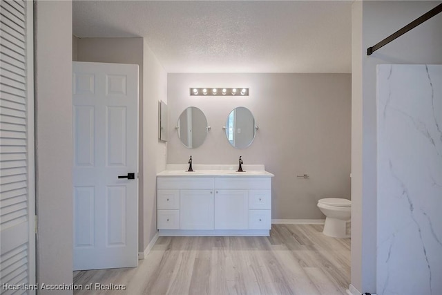 full bathroom with vanity, toilet, baseboards, a textured ceiling, and wood finished floors