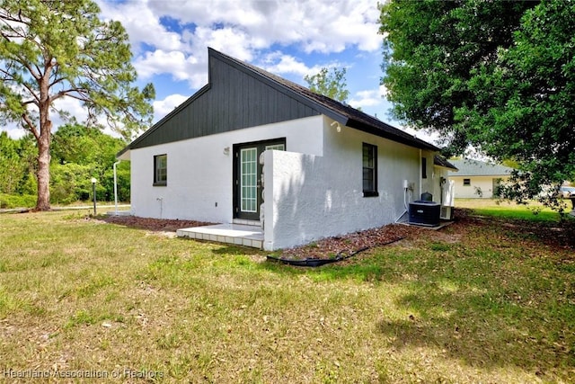 back of property featuring stucco siding, a yard, and central air condition unit