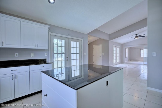 kitchen with light tile patterned floors, dark stone countertops, white cabinetry, french doors, and lofted ceiling
