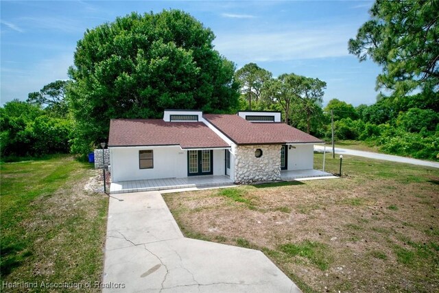 view of front of property with a shingled roof, driveway, stone siding, french doors, and a front lawn