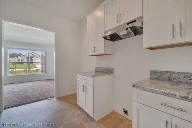 kitchen featuring light stone counters, white cabinets, and light colored carpet