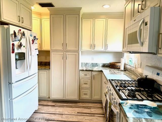 kitchen featuring light stone countertops, white appliances, light hardwood / wood-style flooring, and cream cabinets