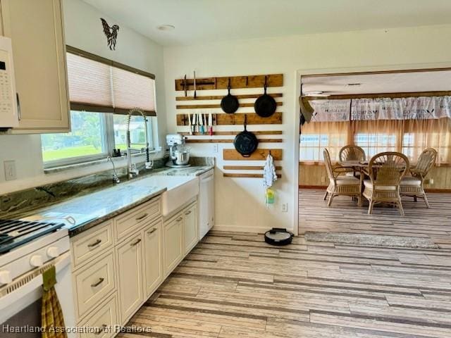 kitchen featuring dishwasher, white stove, sink, light stone countertops, and light wood-type flooring