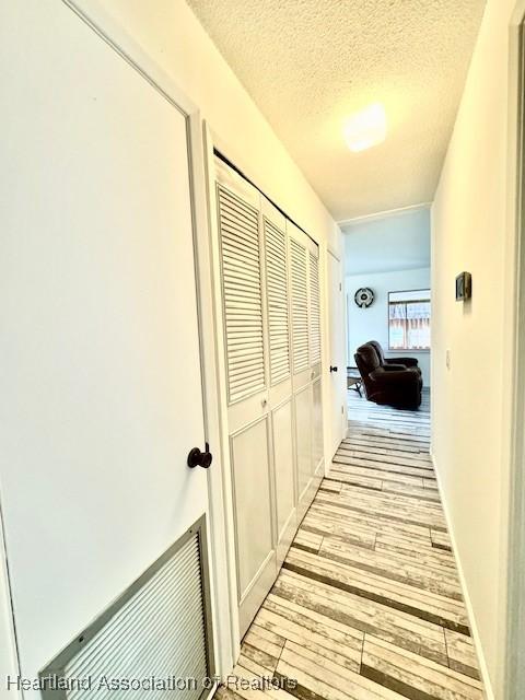 hall with light hardwood / wood-style floors and a textured ceiling