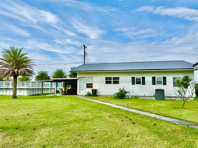 rear view of house featuring a yard, central AC unit, and a carport