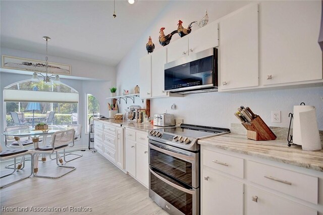 kitchen featuring lofted ceiling, white cabinets, hanging light fixtures, light stone countertops, and appliances with stainless steel finishes