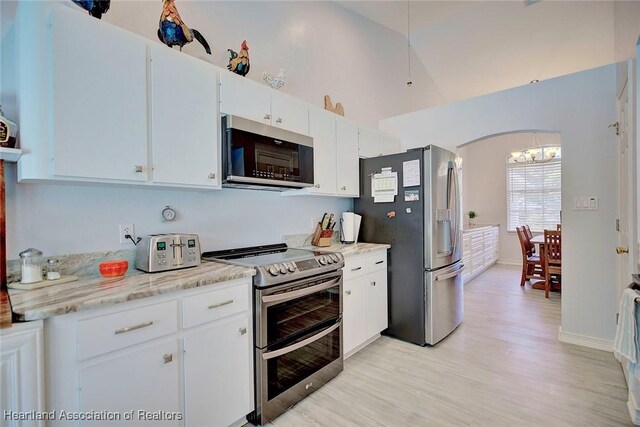 kitchen featuring high vaulted ceiling, white cabinets, light wood-type flooring, appliances with stainless steel finishes, and light stone counters