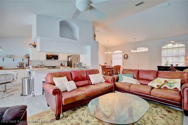 living room featuring light hardwood / wood-style flooring, high vaulted ceiling, and ceiling fan with notable chandelier