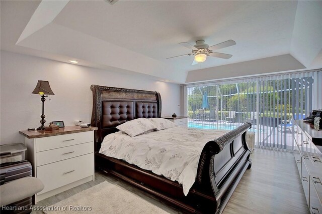 bedroom featuring light wood-type flooring, access to outside, a raised ceiling, and ceiling fan