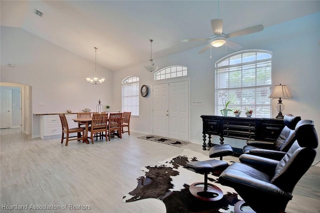 living room with light wood-type flooring, ceiling fan with notable chandelier, and high vaulted ceiling