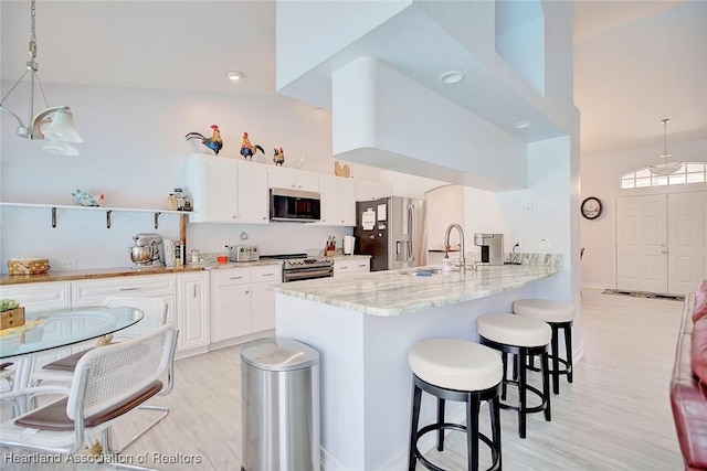 kitchen with light stone countertops, white cabinetry, hanging light fixtures, a breakfast bar, and appliances with stainless steel finishes