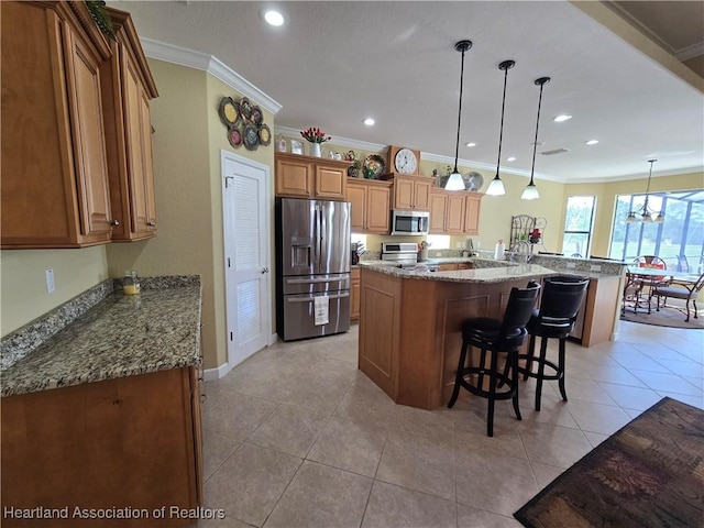 kitchen featuring appliances with stainless steel finishes, ornamental molding, light stone countertops, an island with sink, and decorative light fixtures