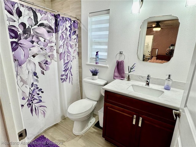 bathroom with walk in shower, ceiling fan, vanity, and toilet