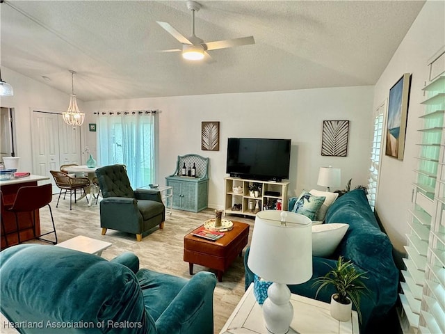 living room with ceiling fan with notable chandelier, light hardwood / wood-style floors, a textured ceiling, and vaulted ceiling