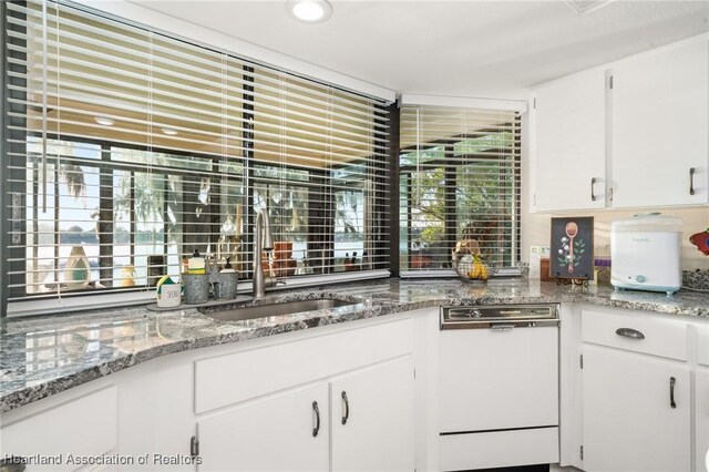 kitchen featuring white cabinets, dishwasher, a sink, and light stone countertops