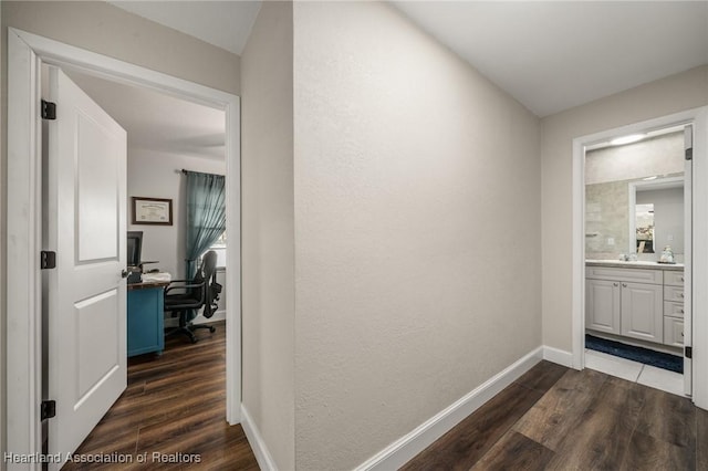 hall with dark wood-type flooring, a sink, and baseboards