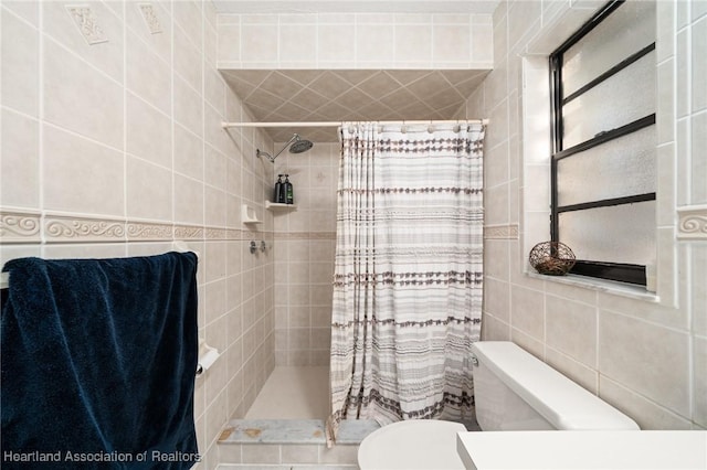 bathroom featuring toilet, tiled shower, and tile walls