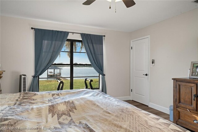 bedroom featuring a water view, ceiling fan, baseboards, and wood finished floors