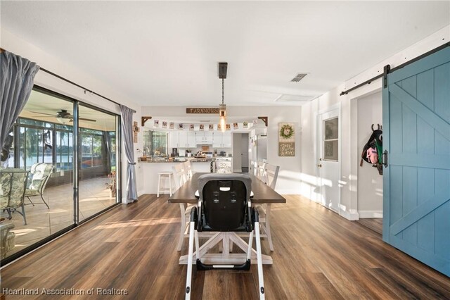 dining space with ceiling fan, a barn door, dark wood-style flooring, visible vents, and baseboards