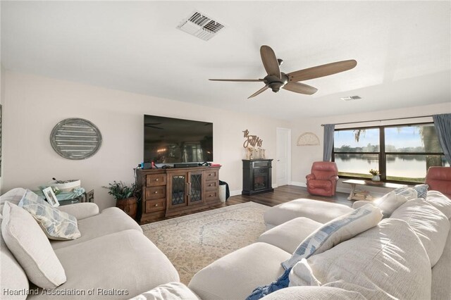 living area with a ceiling fan, wood finished floors, visible vents, and baseboards