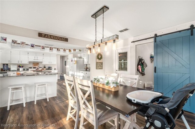 dining room with a barn door, visible vents, and dark wood-style flooring