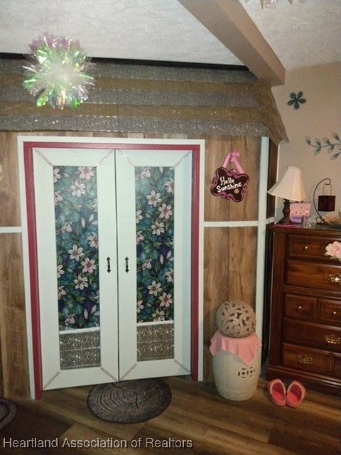 doorway with wood-type flooring, beam ceiling, and a textured ceiling