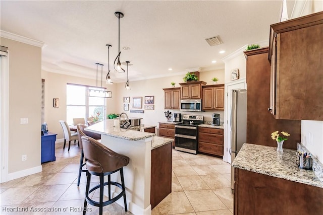 kitchen featuring crown molding, appliances with stainless steel finishes, light stone counters, a center island with sink, and decorative light fixtures