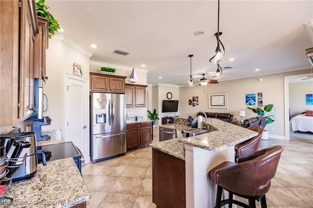 kitchen with ceiling fan, a kitchen island with sink, stainless steel appliances, light stone countertops, and decorative light fixtures