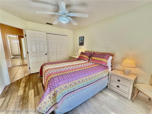 bedroom with a ceiling fan, wood finished floors, visible vents, and a closet