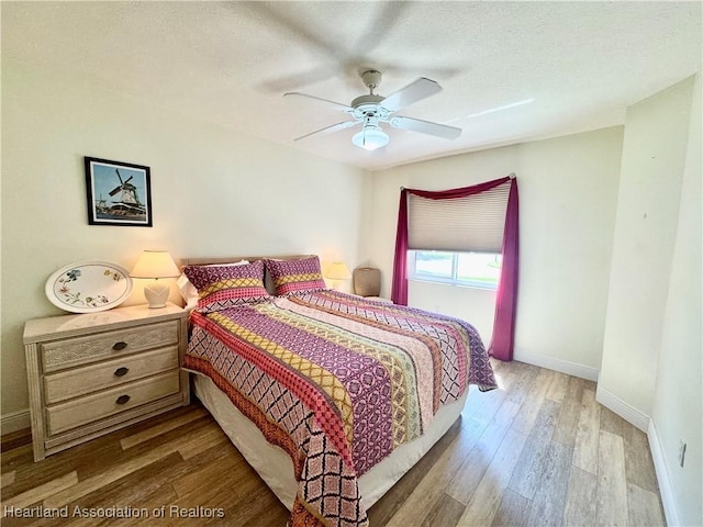 bedroom with ceiling fan, wood finished floors, baseboards, and a textured ceiling