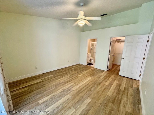 unfurnished bedroom featuring a walk in closet, a textured ceiling, a closet, light wood finished floors, and baseboards