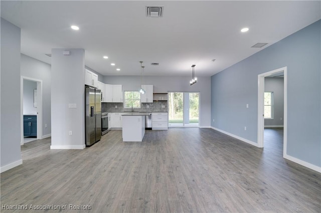 kitchen featuring appliances with stainless steel finishes, light hardwood / wood-style flooring, a center island, white cabinetry, and hanging light fixtures