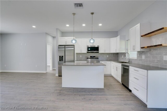 kitchen with stainless steel appliances, sink, decorative light fixtures, white cabinets, and a kitchen island