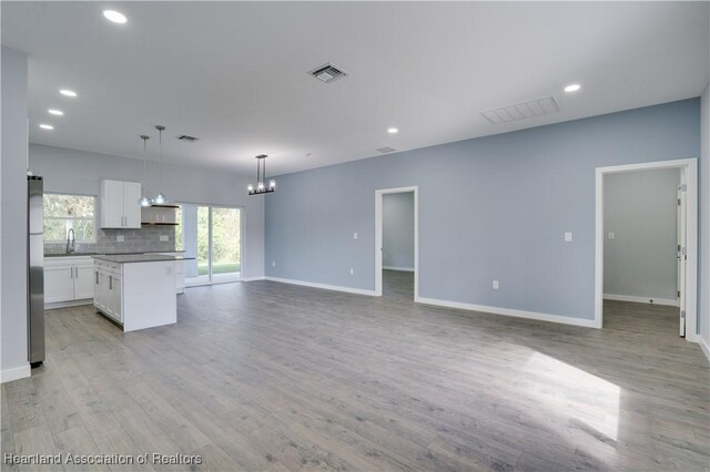 kitchen with tasteful backsplash, pendant lighting, white cabinets, a center island, and stainless steel refrigerator