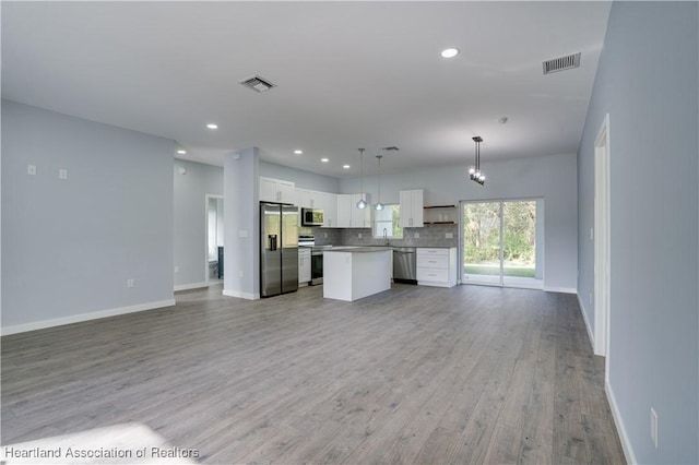 kitchen with appliances with stainless steel finishes, light wood-type flooring, a kitchen island, pendant lighting, and white cabinetry