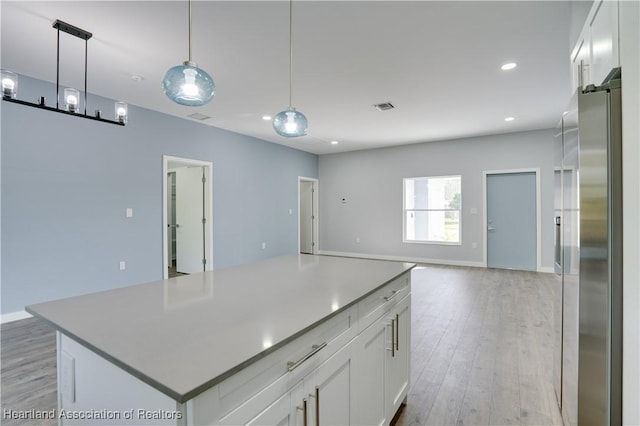 kitchen with stainless steel fridge, white cabinetry, hanging light fixtures, and a kitchen island