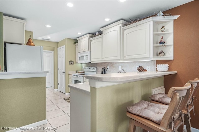 kitchen with kitchen peninsula, white cabinetry, light tile patterned floors, and white appliances