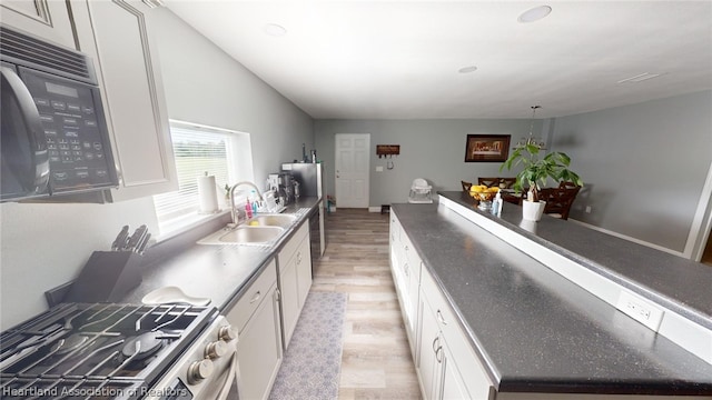 kitchen featuring high end stainless steel range oven, sink, white cabinetry, and light hardwood / wood-style floors