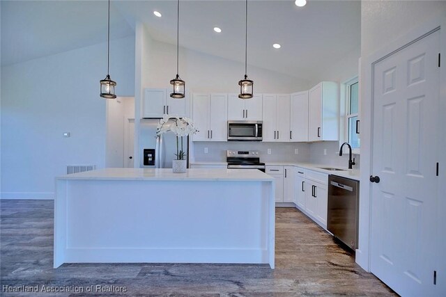 kitchen featuring stainless steel appliances, white cabinets, a kitchen island, a sink, and wood finished floors