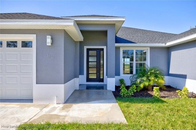 entrance to property featuring a garage, a shingled roof, and stucco siding