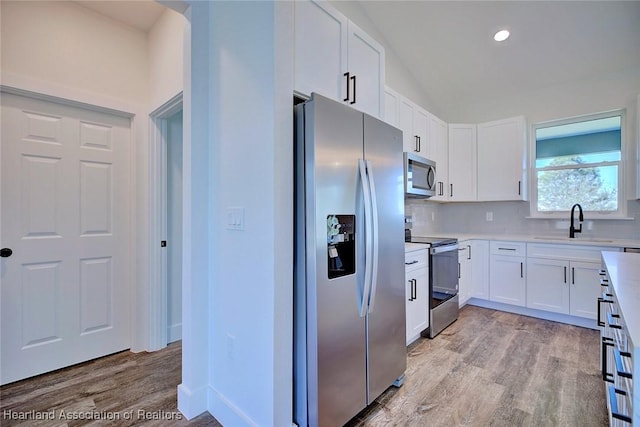 kitchen with light wood finished floors, light countertops, appliances with stainless steel finishes, white cabinetry, and a sink