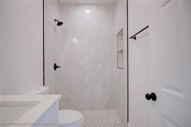 full bathroom featuring tiled shower, vanity, and toilet